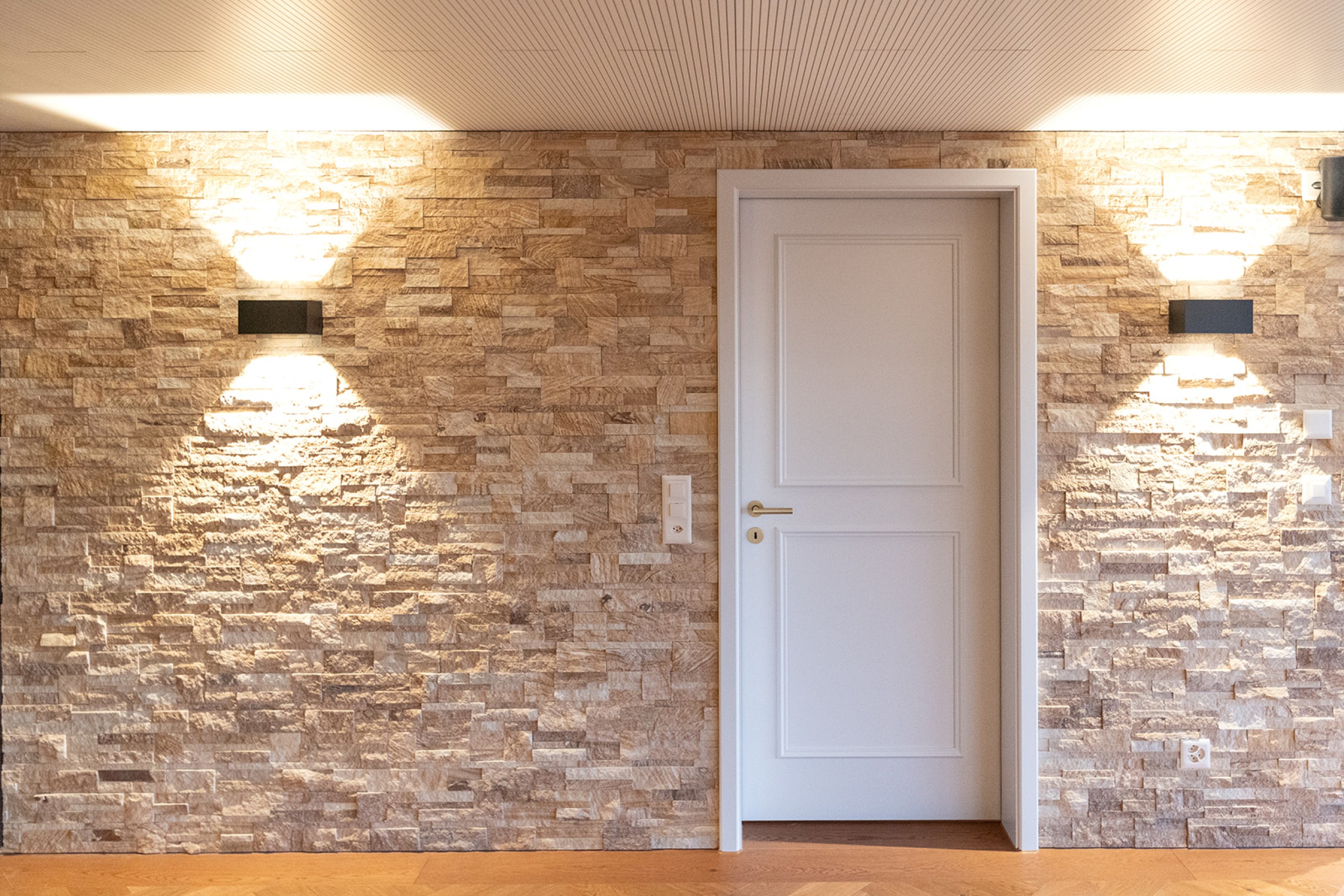 Modernes Untergeschoss mit Home Cinema und Barbereich, kombiniert aus rustikalem Steinmauerwerk und hochwertigen Holzakzenten.