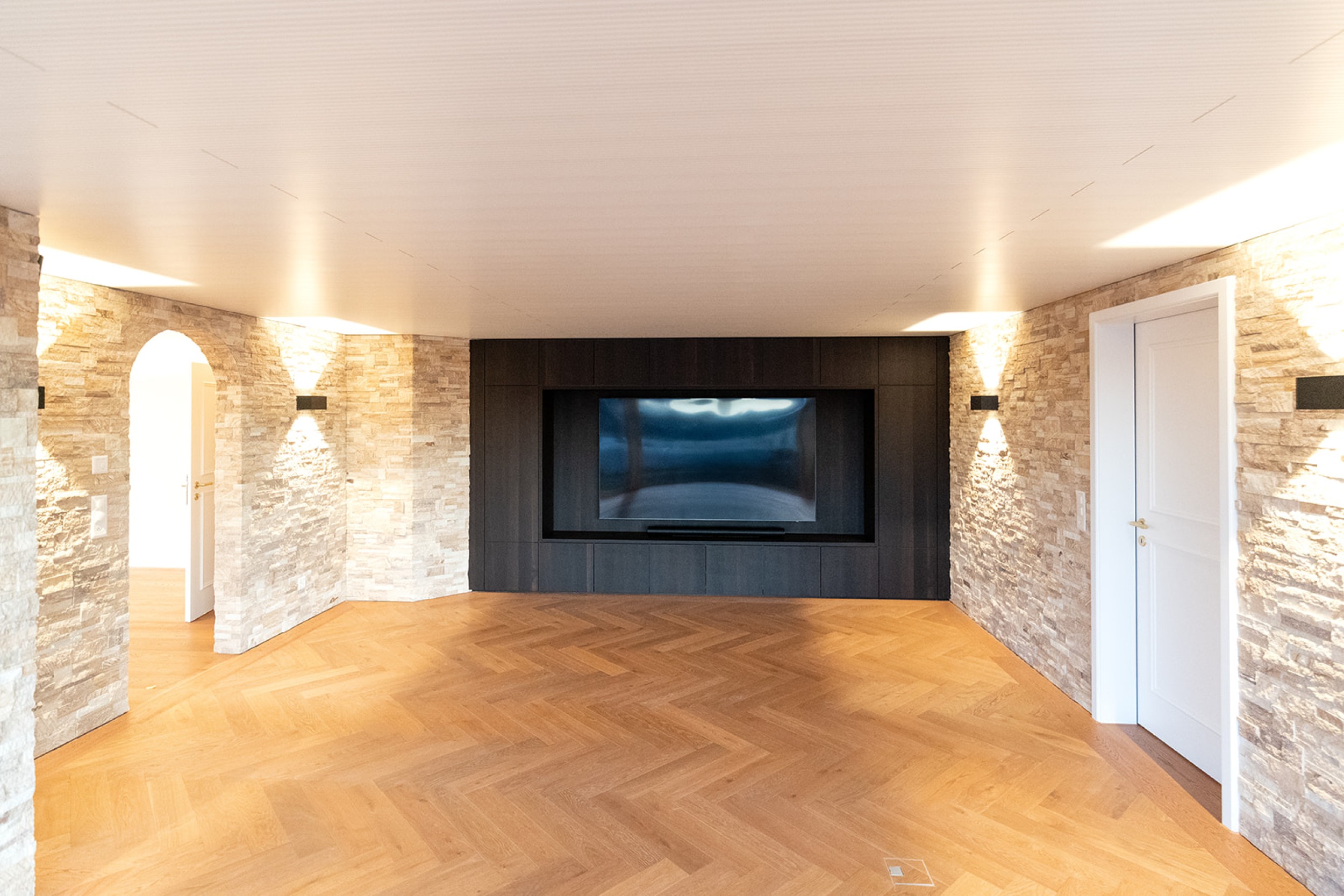 Modernes Untergeschoss mit Home Cinema und Barbereich, kombiniert aus rustikalem Steinmauerwerk und hochwertigen Holzakzenten.