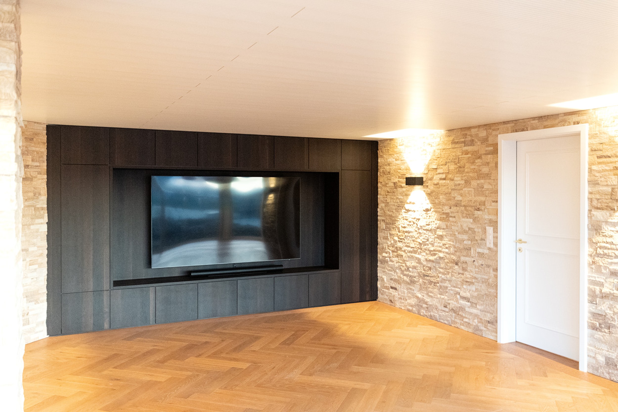 Modernes Untergeschoss mit Home Cinema und Barbereich, kombiniert aus rustikalem Steinmauerwerk und hochwertigen Holzakzenten.