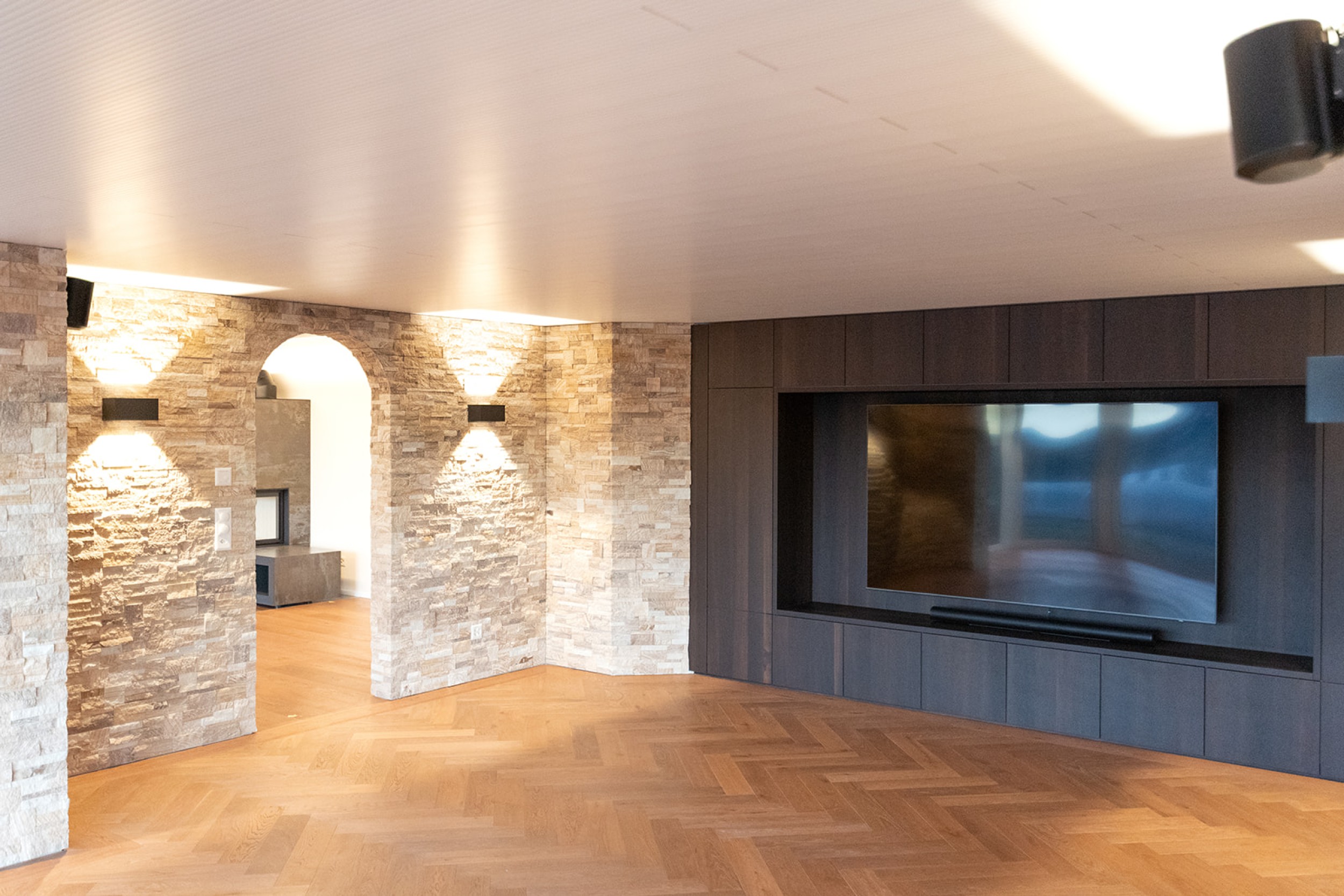 Modernes Untergeschoss mit Home Cinema und Bar, geprägt von rustikalem Steinmauerwerk und elegantem Fischgrat‑Parkett.