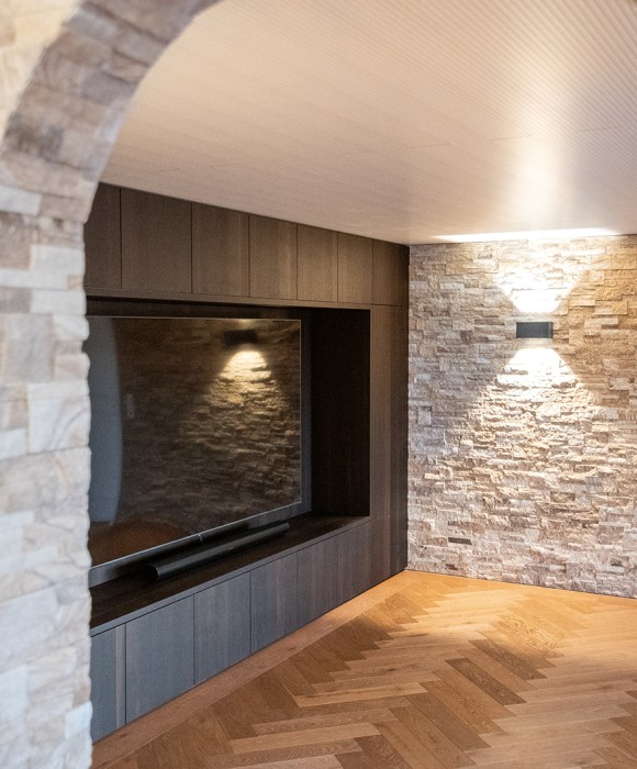 Modernes Untergeschoss mit Home Cinema und Bar, geprägt von rustikalem Steinmauerwerk und elegantem Fischgrat‑Parkett.