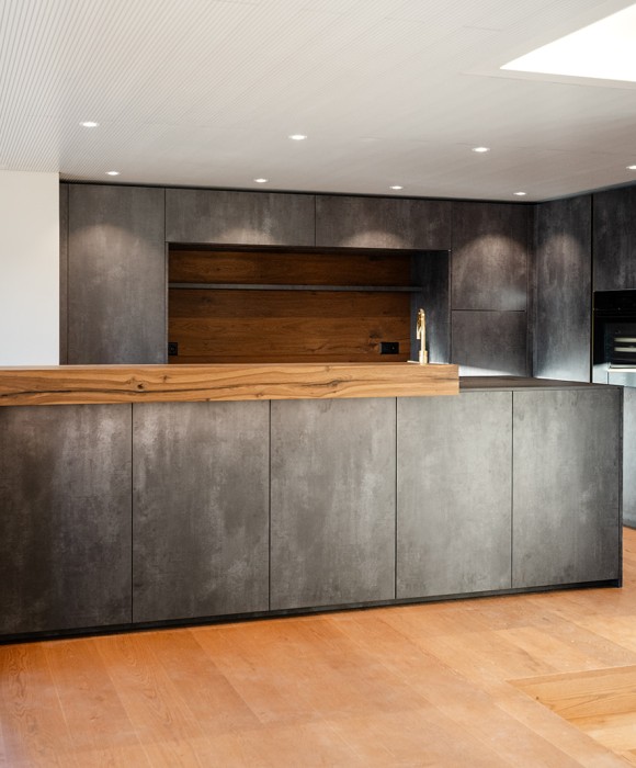 Moderne Küche mit grosszügiger Arbeitsfläche, integrierten Geräten und einer Kombination aus glatten Oberflächen und warmen Holzelementen.