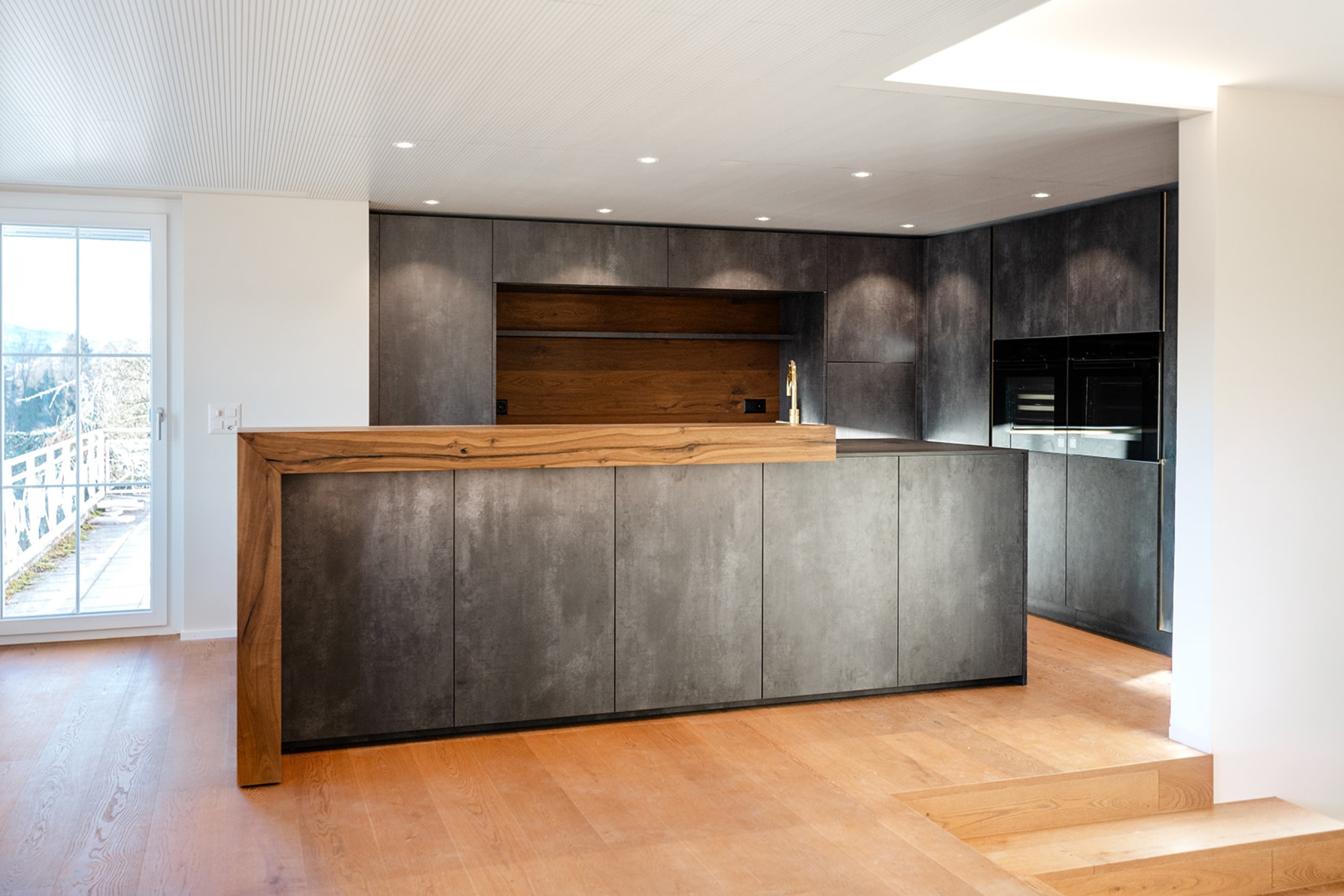 Moderne Küche mit grosszügiger Arbeitsfläche, integrierten Geräten und einer Kombination aus glatten Oberflächen und warmen Holzelementen.