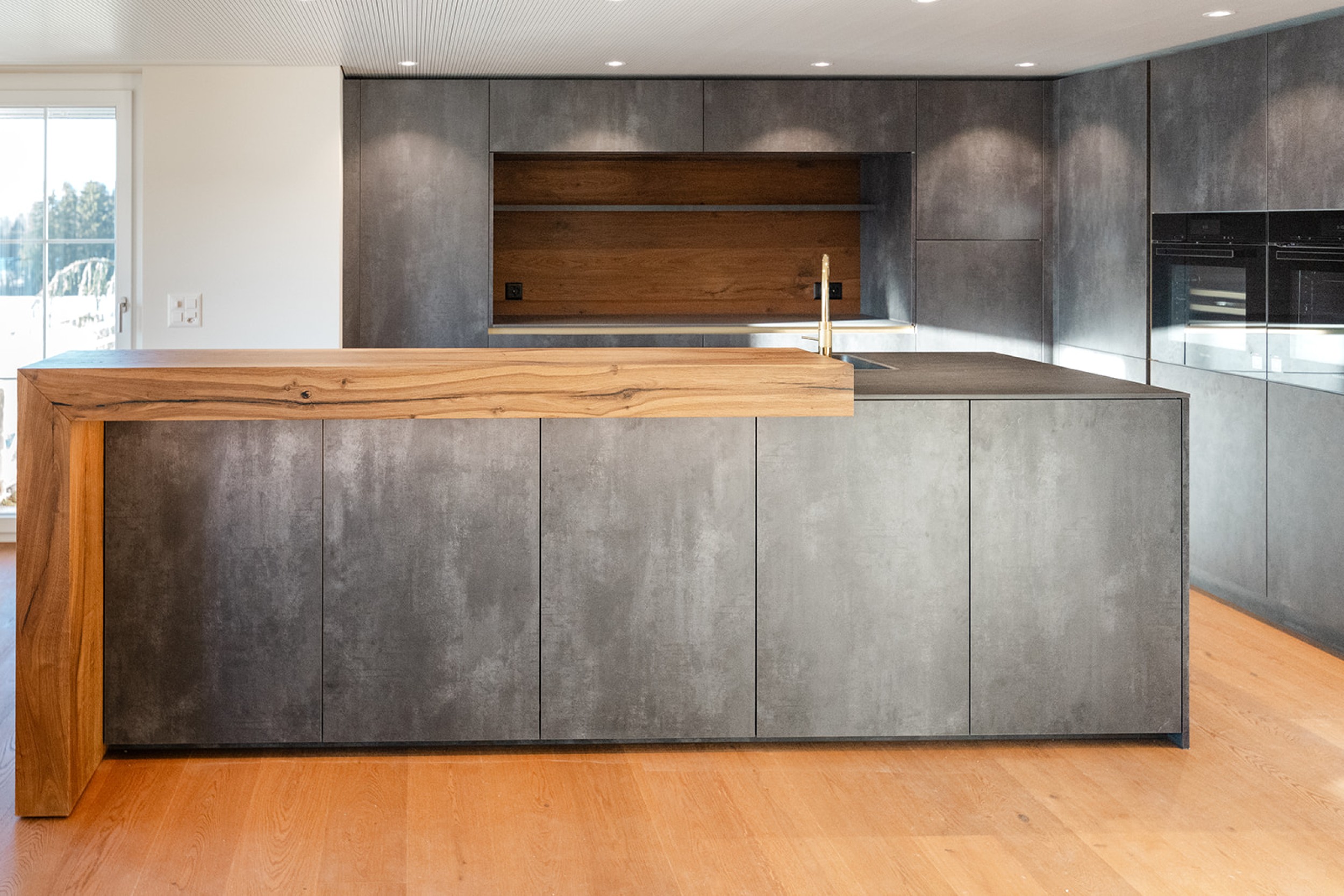 Moderne Küche mit grosszügiger Arbeitsfläche, integrierten Geräten und einer Kombination aus glatten Oberflächen und warmen Holzelementen.